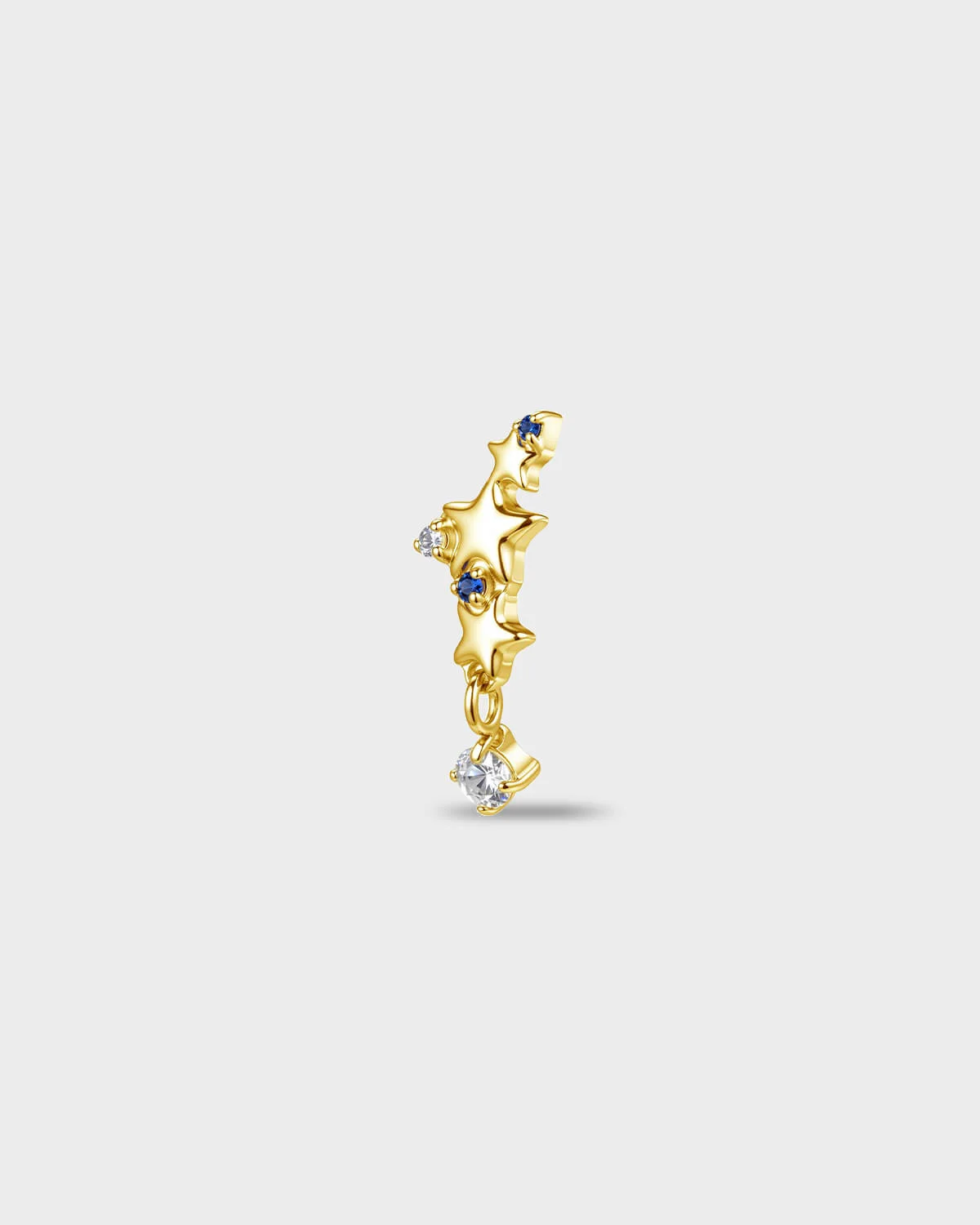 Gold titanium earring with a row of star shapes set with blue and clear round-cut stones, finished with a short dangle and a clear round-cut stone, on a light gray background.