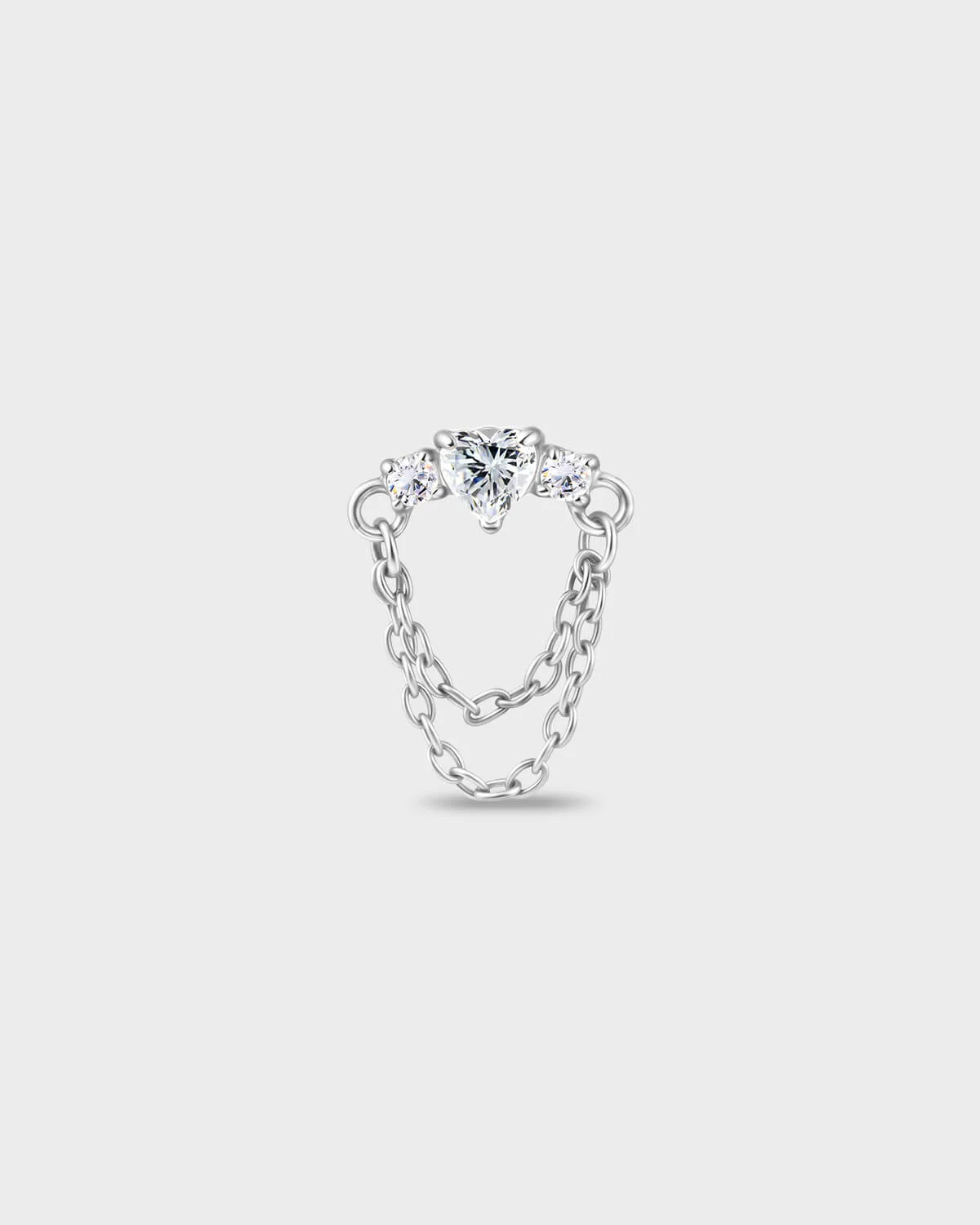 Polished titanium earring with a heart-cut clear stone set between two smaller round-cut stones, finished with a double chain detail on a light gray background.