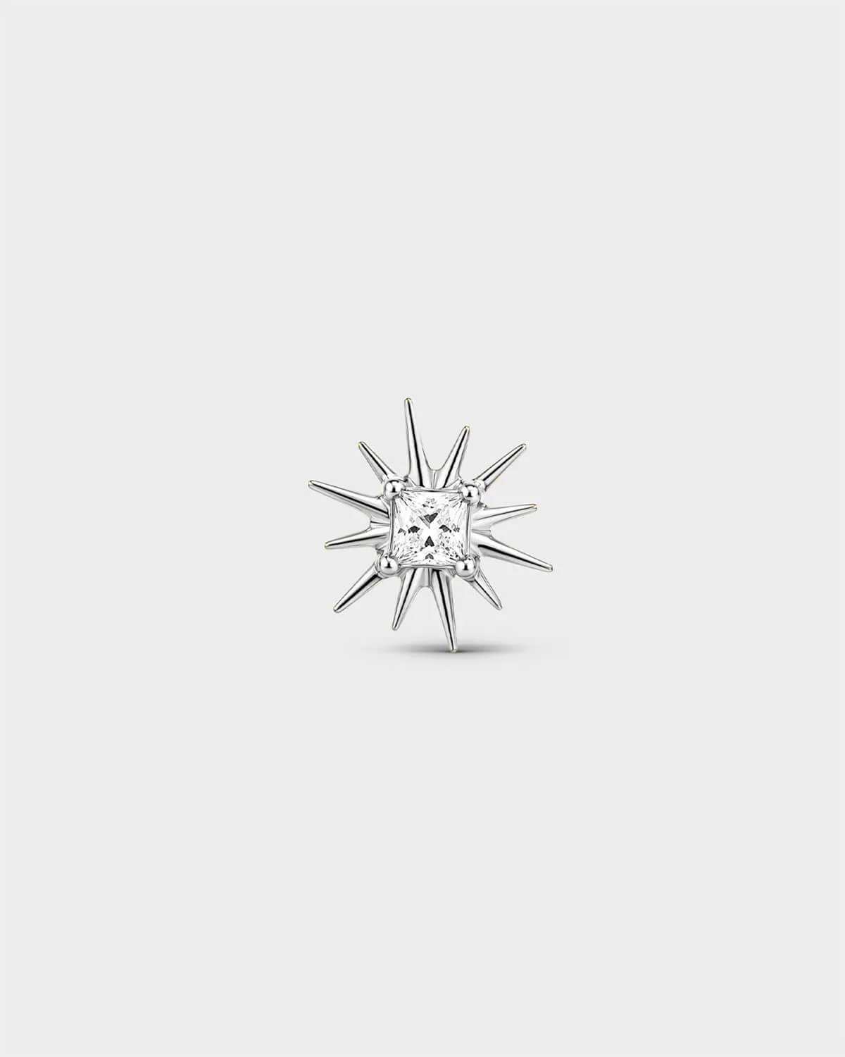 Polished silver titanium threadless end with a princess-cut clear stone set within a sculpted starburst design. On a light grey background.