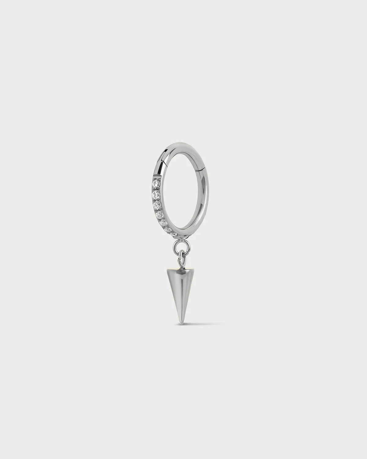 Polished silver titanium hinged ring with pave gems around the outer edge and a single cone dangle charm sat on a light gray background.