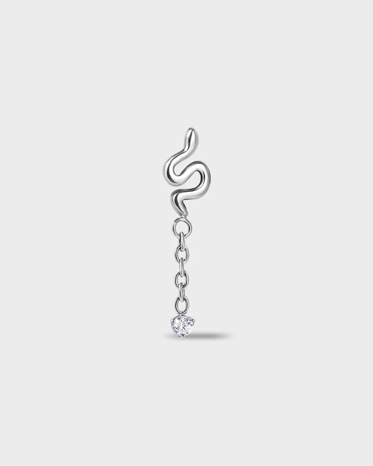Polished silver titanium earring with a snake-shaped top and a short chain detail, finished with a clear round-cut gem on a light gray background.