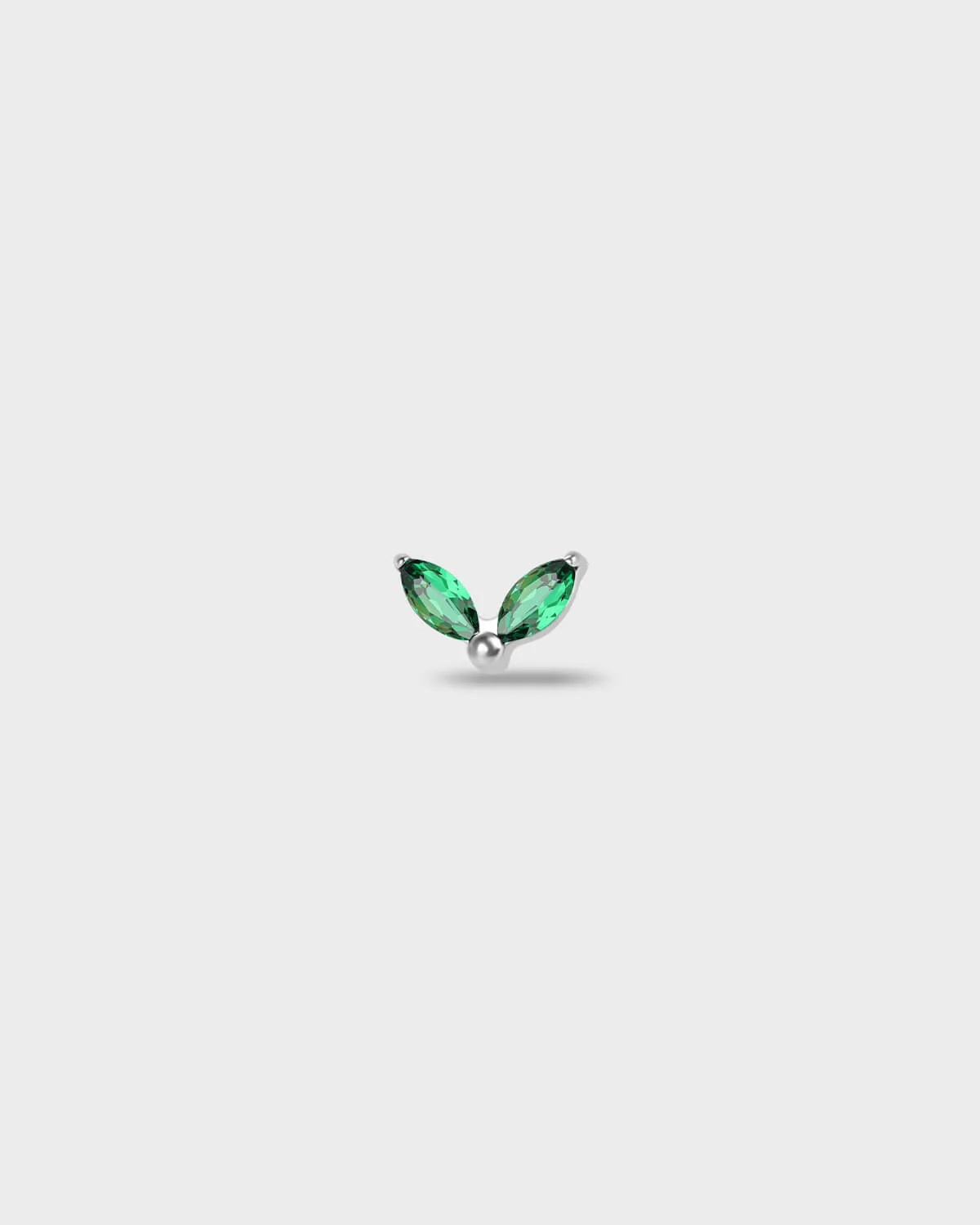 Polished titanium earring with two marquise-cut emerald green stones set in a simple leaf-style arrangement, on a light rgray background.