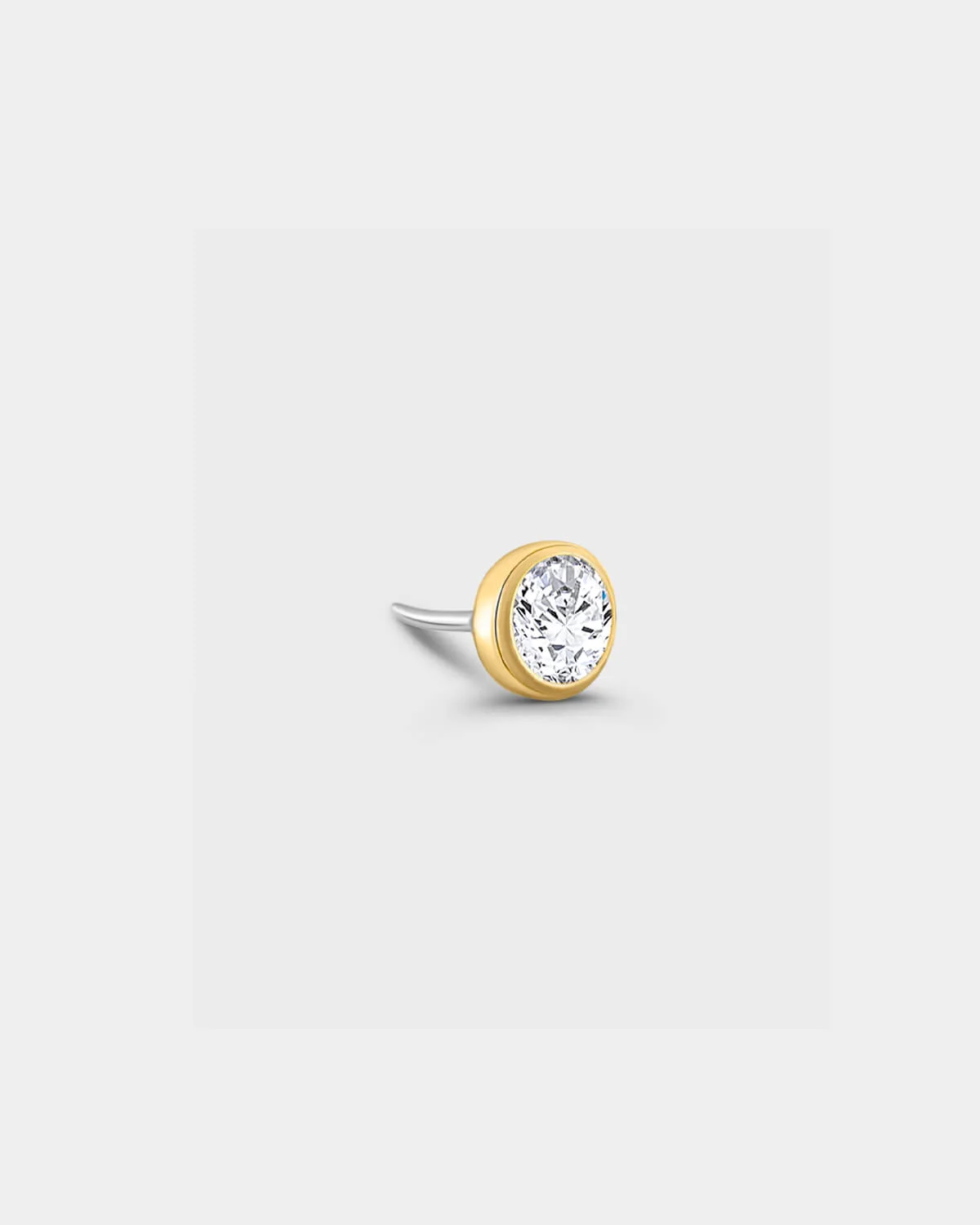 Gold titanium bezel set solitaire with clear gemstone n a light grey background.