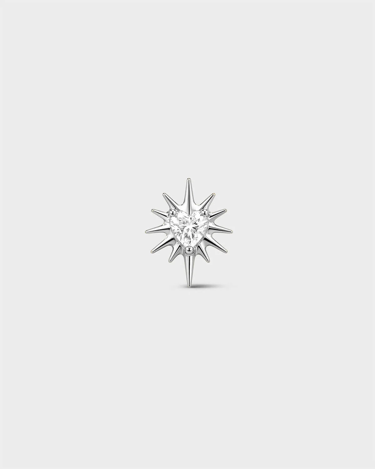 Polished titanium threadless end earring with a heart-cut clear stone set within a sculpted starburst design. On a light grey background.