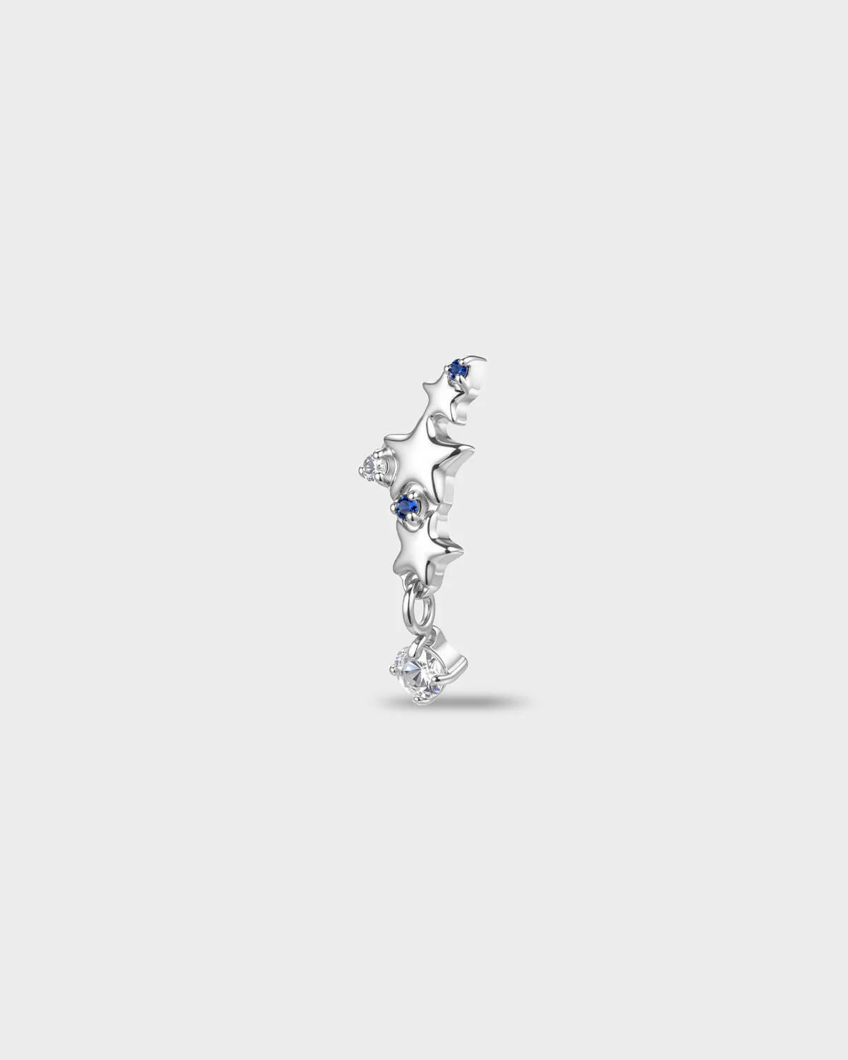 Polished titanium earring with a row of star shapes set with blue and clear round-cut stones, finished with a short dangle and a clear round-cut stone, on a light gray background.