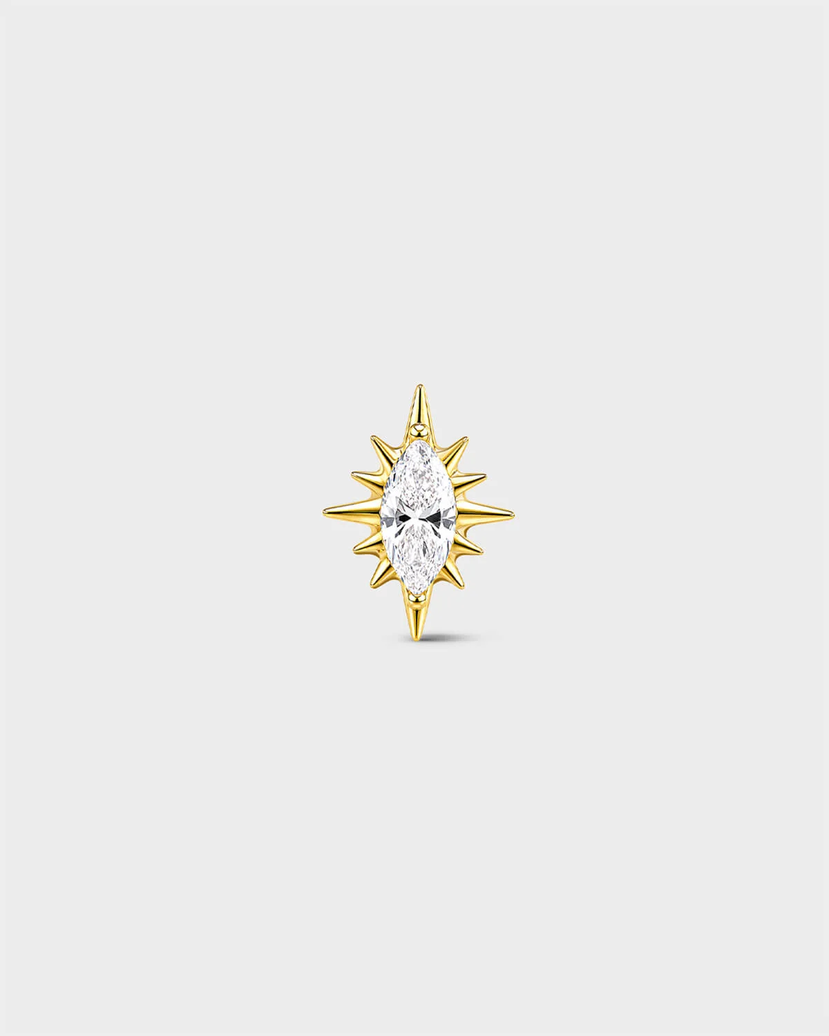 Gold titanium threadless end earring with a marquise-cut clear stone set within a sculpted starburst design. On a light grey background.