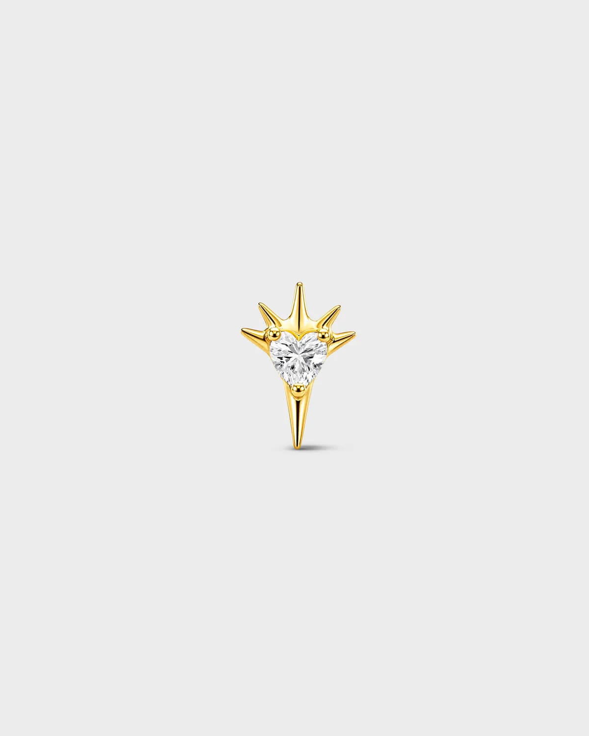 Gold titanium threadless end earring with a heart-cut clear stone set within a sculpted starburst design. On a light grey background.