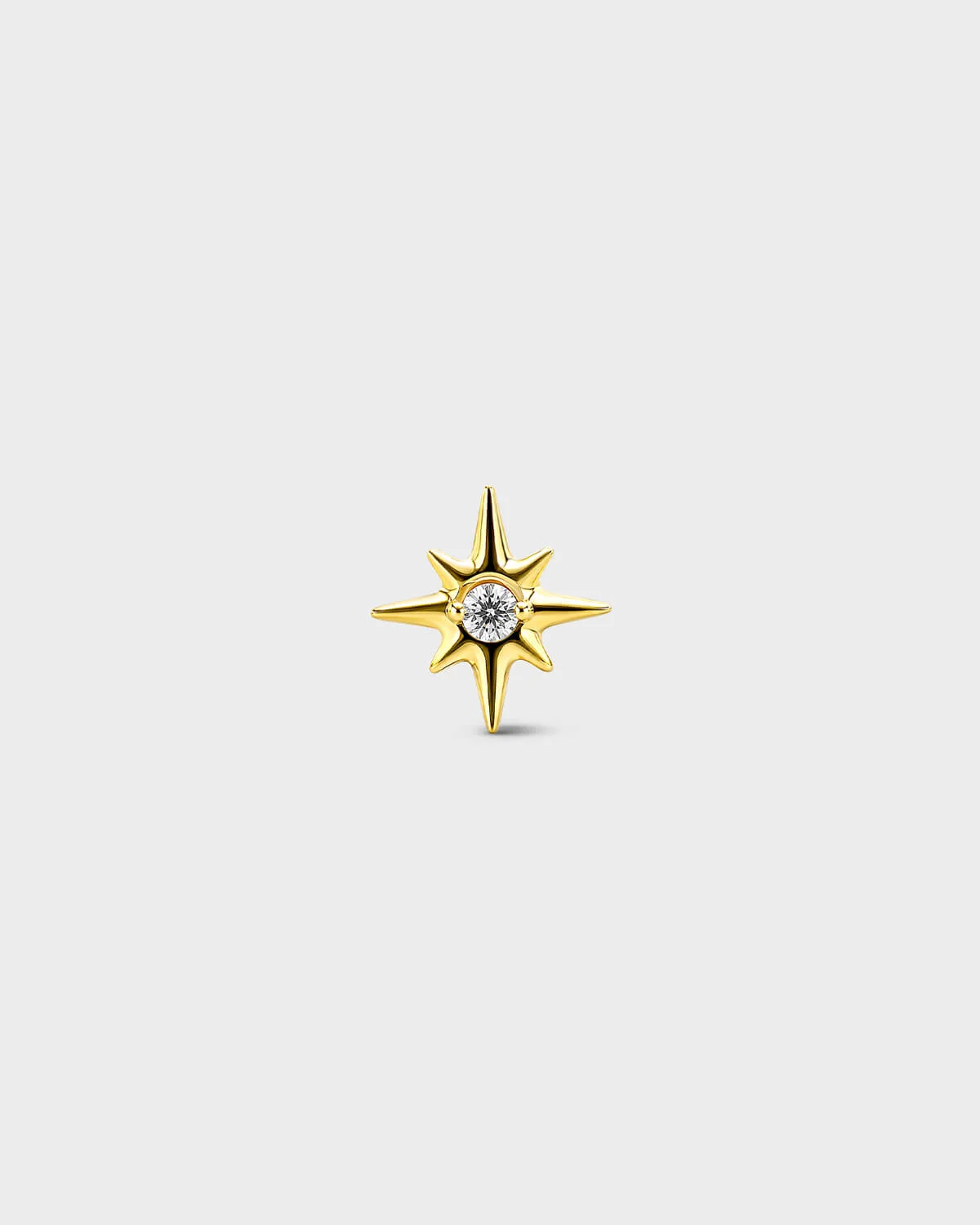Gold titanium threadless end earring with a round-cut clear stone set within a sculpted star design. On a light grey background.