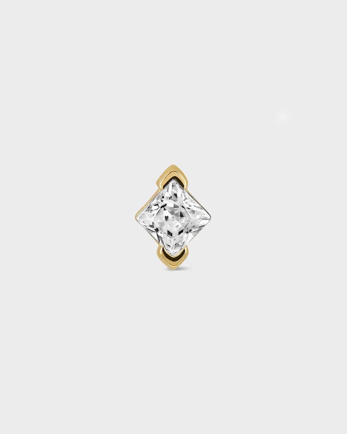 Gold earring with a clear gemstone on a light gray background