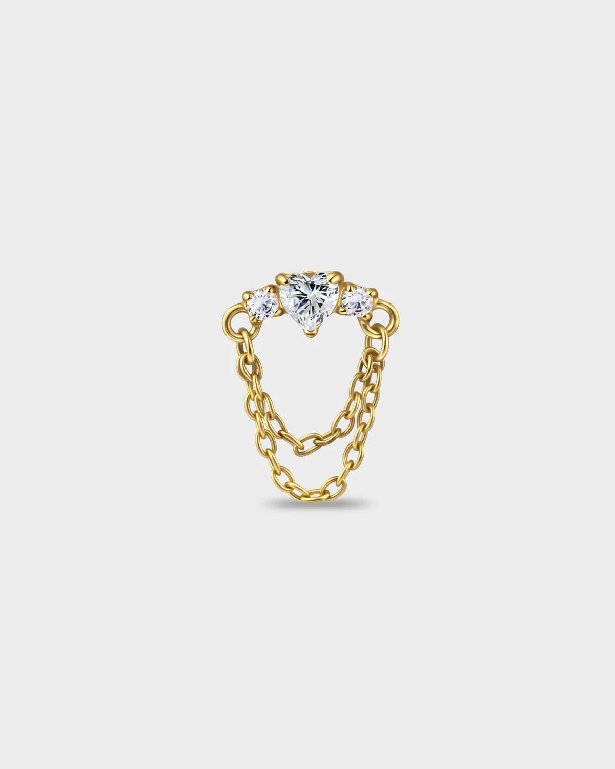 Gold titanium earring with a heart-cut clear stone set between two smaller round-cut stones, finished with a double chain detail on a light gray background.