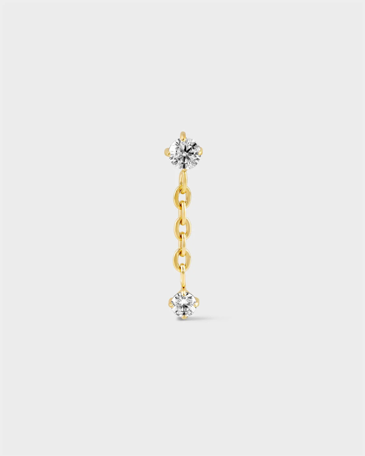 Gold titanium earring with solitaire and chain dropping to another smaller solitaire on a light grey background.