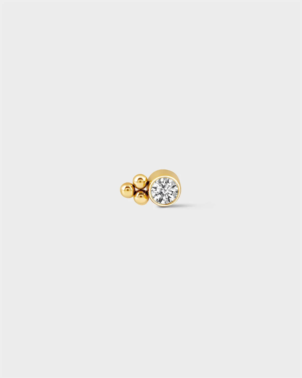 24k gold titanium bezel set solitaire earring with 3 beads detail to one side on a light grey background.