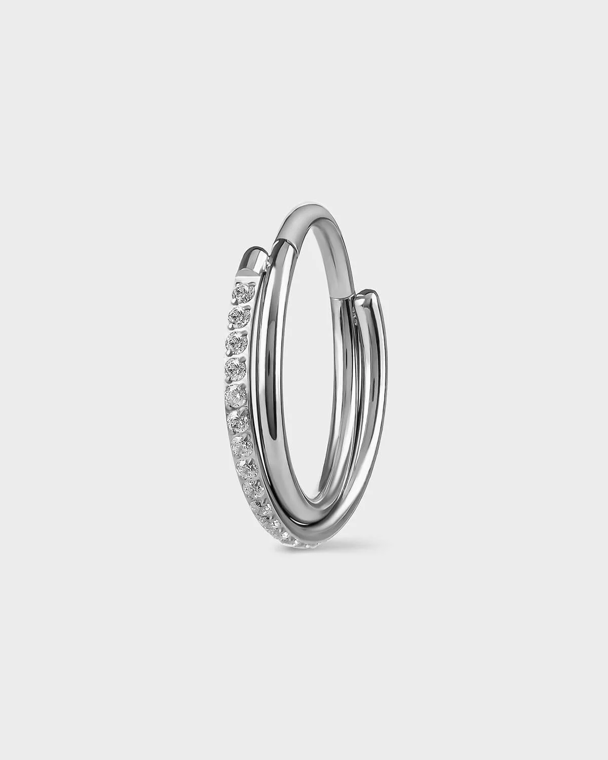 Polished silver titanium with double twist ring. One pave and the other plain. Clear gemstones. Sat on a light gray backround.