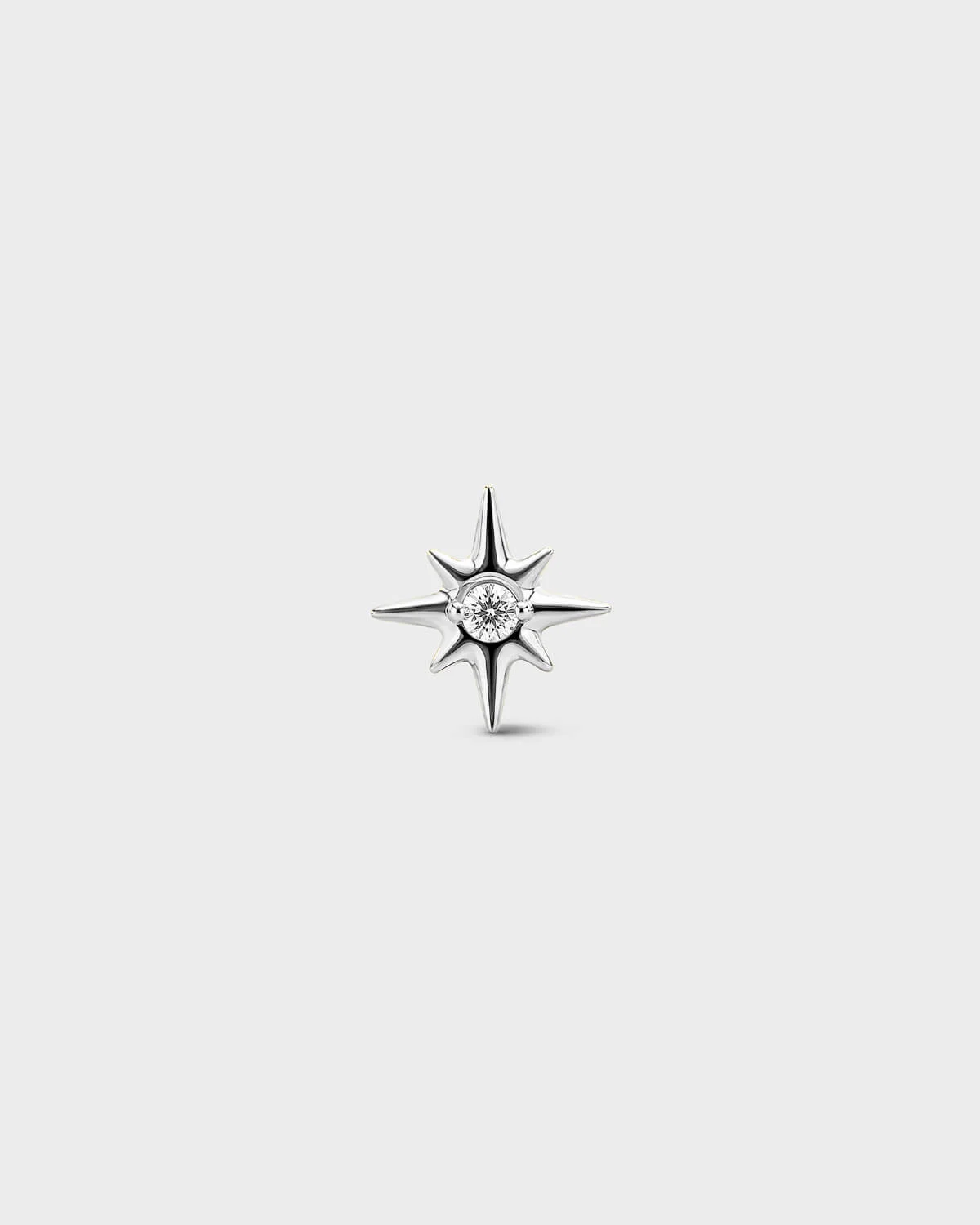 Gold titanium threadless end earring with a round-cut clear stone set within a sculpted star design. On a light grey background.