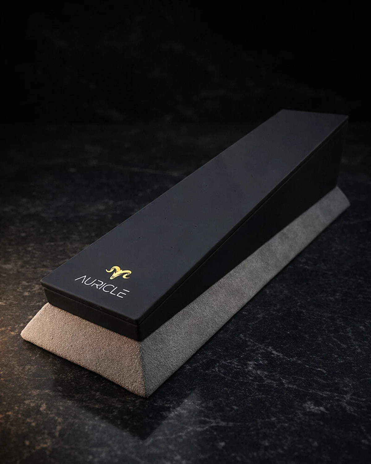 jewellery display stand to hold 20 pieces of jewellery. The stand has a light gray suede base with a black leather top. Sat on a dark worktop with moody lighting.